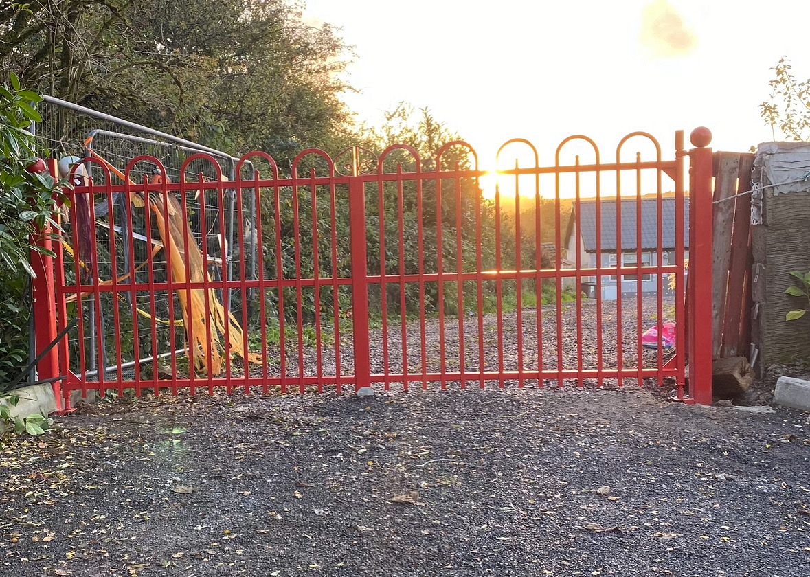 Red powder-coated steel sliding gate with arched top and ball finial